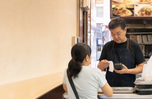 香港小食店店主在櫃檯以付款終端和訂單紙核對顧客付款流程