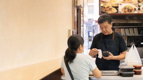 香港小食店店主在櫃檯以付款終端和訂單紙核對顧客付款流程