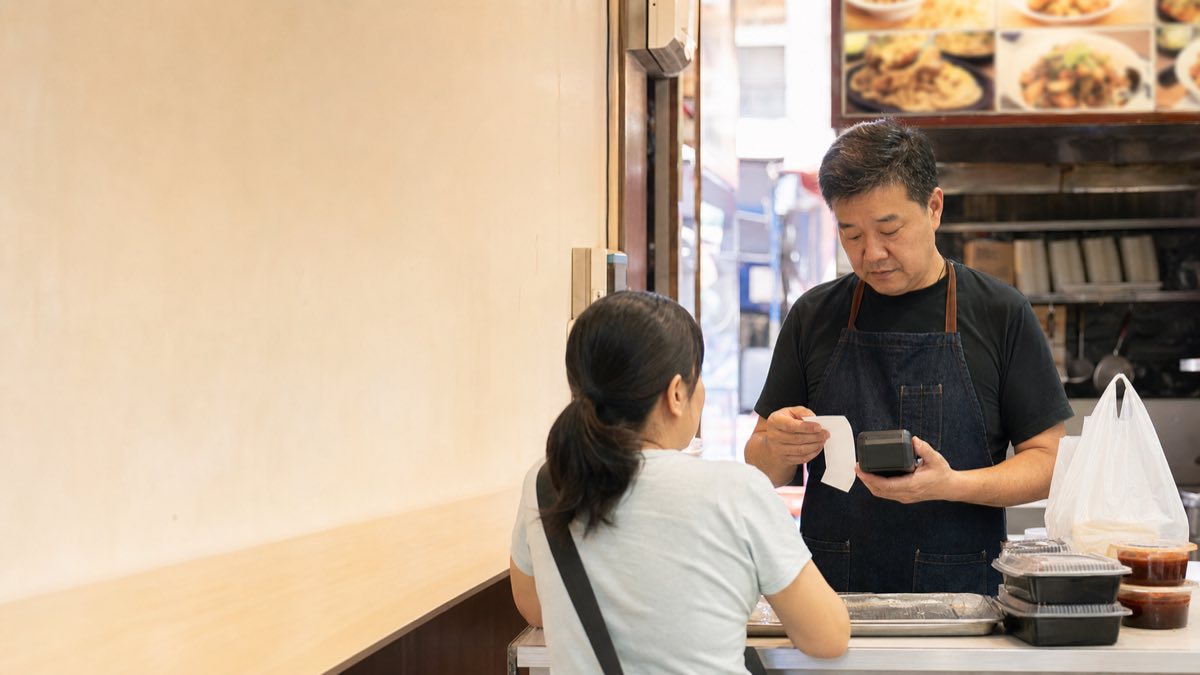 香港小食店店主在櫃檯以付款終端和訂單紙核對顧客付款流程